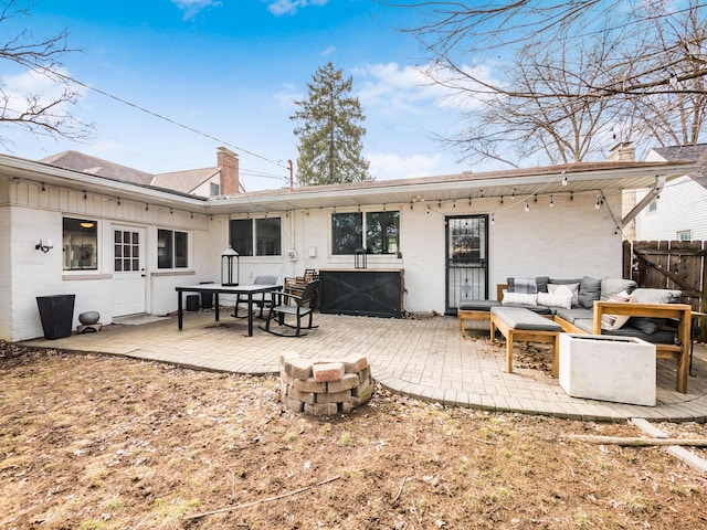 rear view of property featuring an outdoor living space with a fire pit, a patio, a chimney, fence, and brick siding