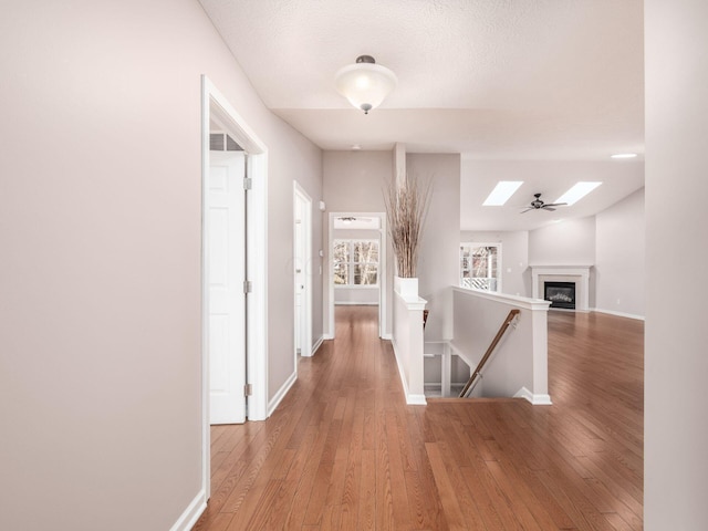 hallway featuring a skylight, an upstairs landing, light wood-style floors, and baseboards