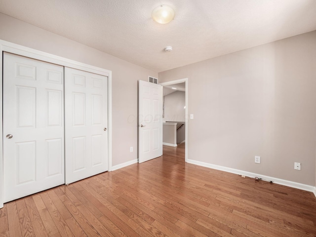 unfurnished bedroom featuring light wood-style flooring, baseboards, visible vents, and a closet