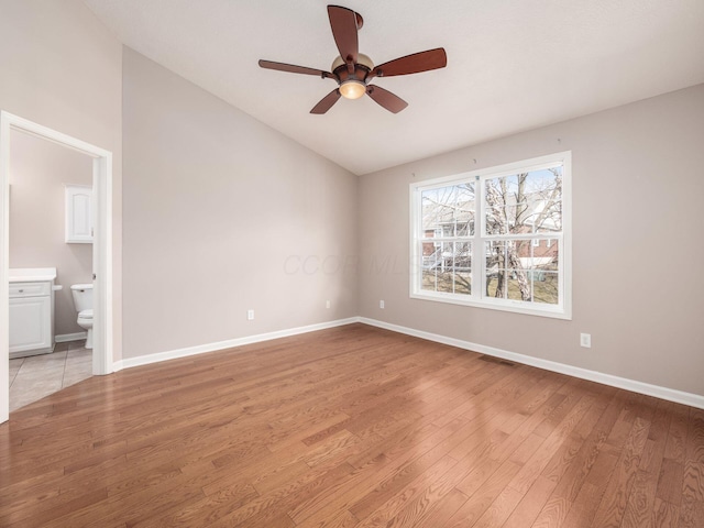 unfurnished bedroom featuring visible vents, baseboards, light wood-type flooring, lofted ceiling, and ensuite bath