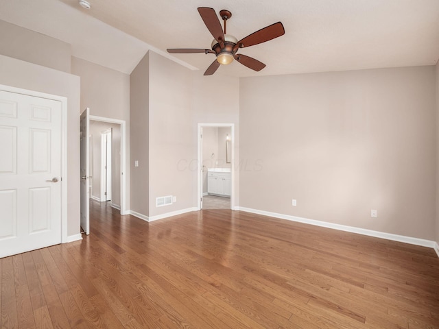 unfurnished bedroom featuring visible vents, baseboards, vaulted ceiling, wood finished floors, and ensuite bath