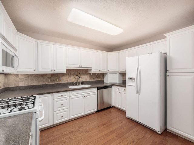 kitchen with dark countertops, light wood finished floors, white appliances, white cabinetry, and a sink