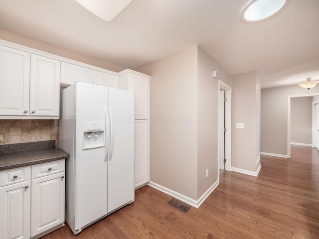 kitchen featuring visible vents, dark countertops, white refrigerator with ice dispenser, light wood-style floors, and white cabinets