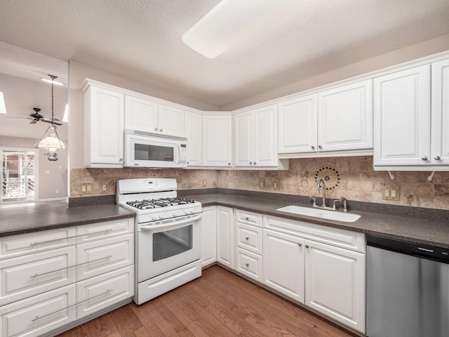 kitchen featuring dark countertops, white appliances, wood finished floors, and a sink