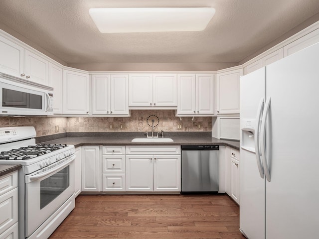 kitchen with dark countertops, wood finished floors, white appliances, white cabinetry, and a sink