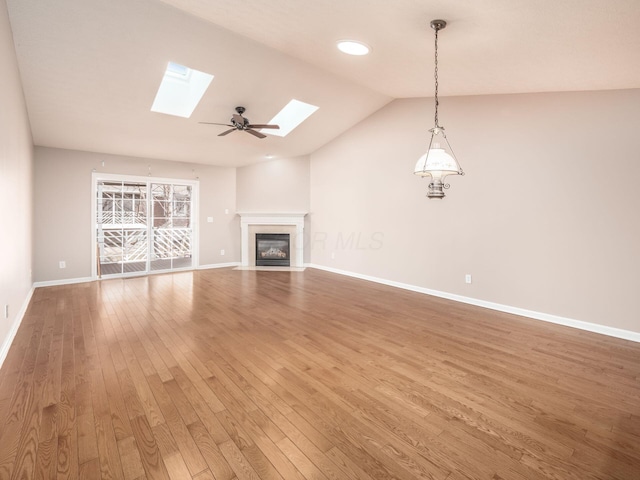 unfurnished living room with light wood finished floors, baseboards, lofted ceiling with skylight, a fireplace with flush hearth, and a ceiling fan