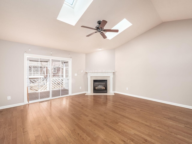 unfurnished living room featuring ceiling fan, baseboards, lofted ceiling with skylight, a fireplace with flush hearth, and wood finished floors