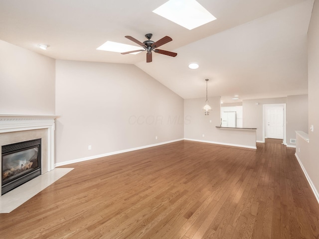 unfurnished living room featuring ceiling fan, baseboards, lofted ceiling with skylight, a fireplace, and wood finished floors