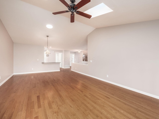 unfurnished living room featuring vaulted ceiling with skylight, wood finished floors, baseboards, and ceiling fan