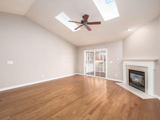 unfurnished living room with baseboards, a fireplace with flush hearth, ceiling fan, light wood-style floors, and lofted ceiling with skylight