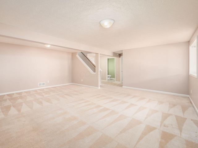 unfurnished room with stairs, a textured ceiling, baseboards, and light carpet