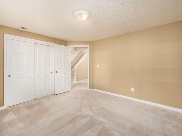 unfurnished bedroom with visible vents, a textured ceiling, a closet, carpet, and baseboards