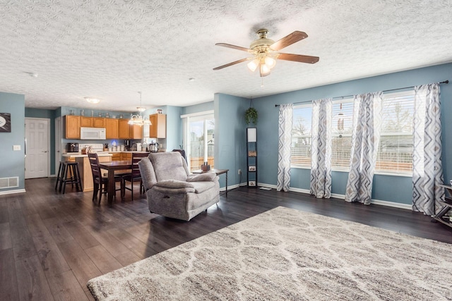 living area with ceiling fan with notable chandelier, dark wood-type flooring, and baseboards