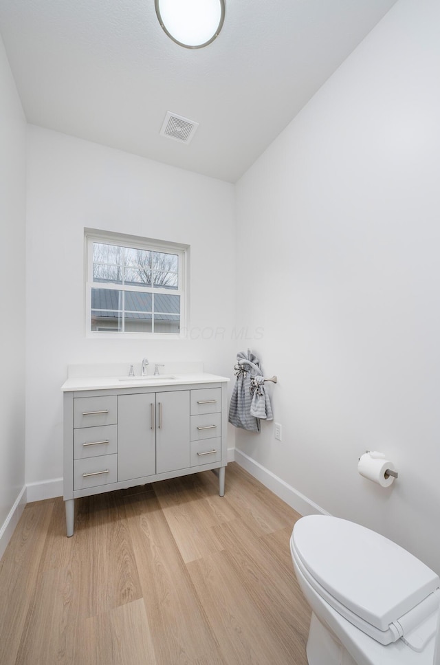 bathroom with visible vents, toilet, vanity, wood finished floors, and baseboards