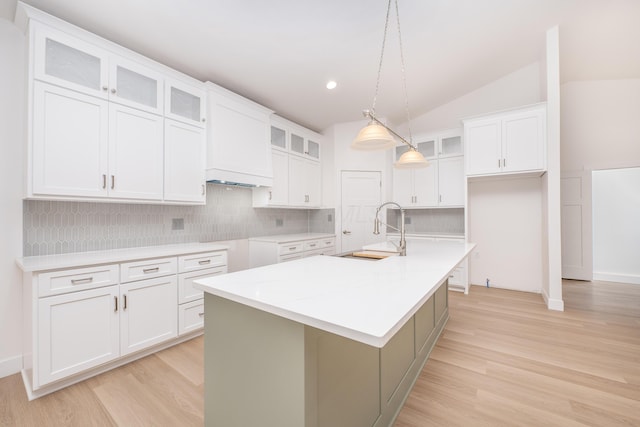 kitchen featuring light wood-type flooring, a kitchen island with sink, vaulted ceiling, and a sink