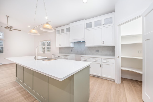 kitchen featuring light wood-style flooring, white cabinetry, a sink, and backsplash