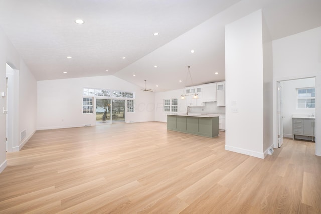 unfurnished living room featuring high vaulted ceiling, baseboards, a sink, and light wood finished floors