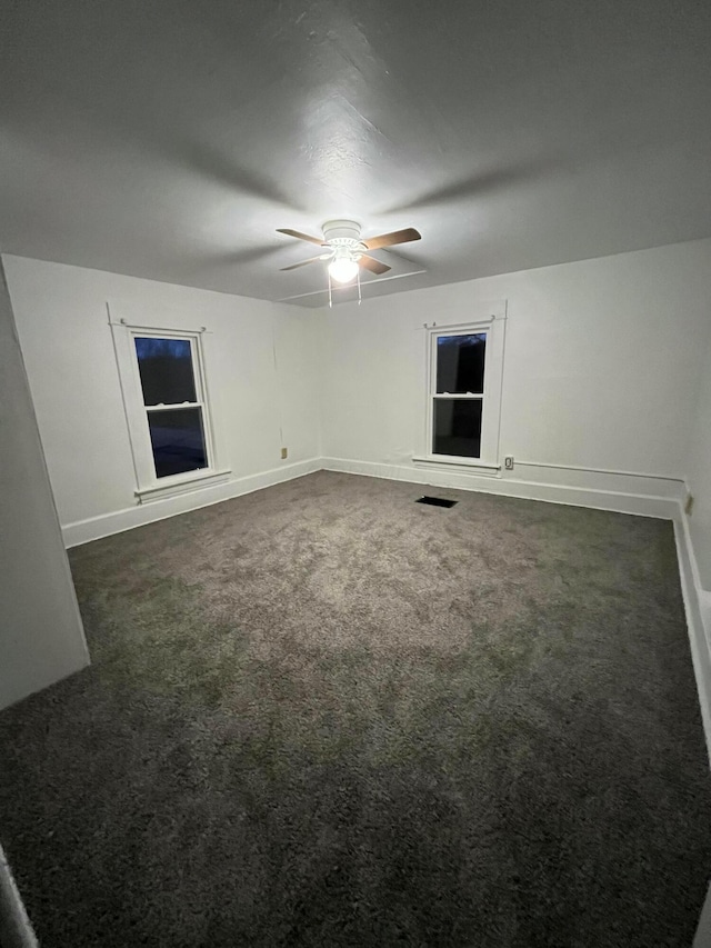 empty room with a ceiling fan, dark colored carpet, and baseboards