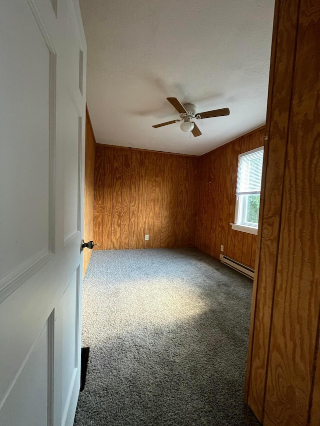 unfurnished room featuring a baseboard heating unit, carpet flooring, wood walls, and ceiling fan