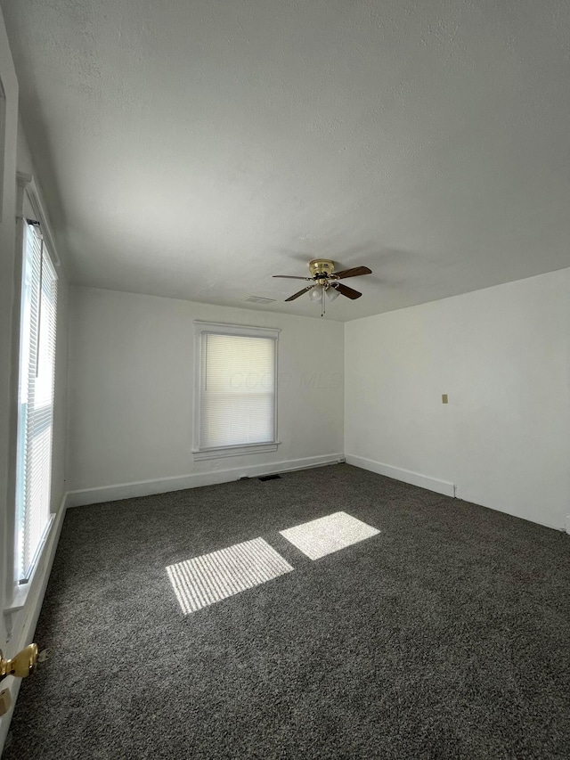 unfurnished room with a textured ceiling, baseboards, and dark colored carpet