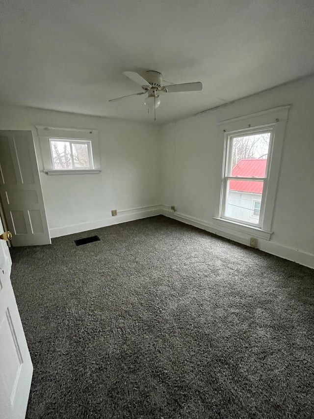 empty room featuring visible vents, dark carpet, baseboards, and ceiling fan