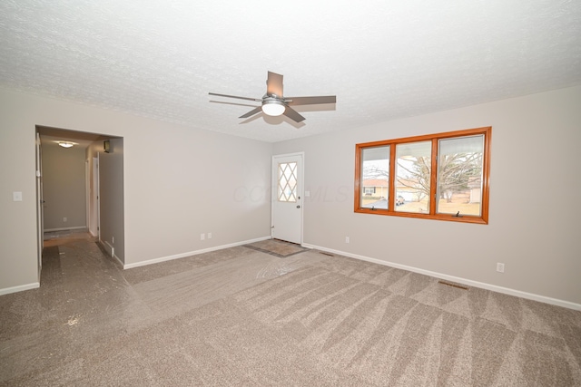 carpeted empty room featuring a textured ceiling, ceiling fan, and baseboards