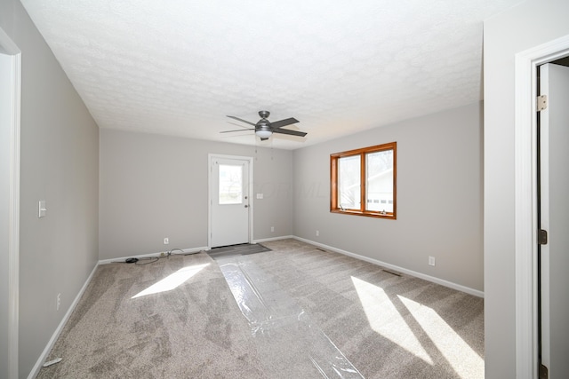 interior space featuring ceiling fan, baseboards, a textured ceiling, and light colored carpet