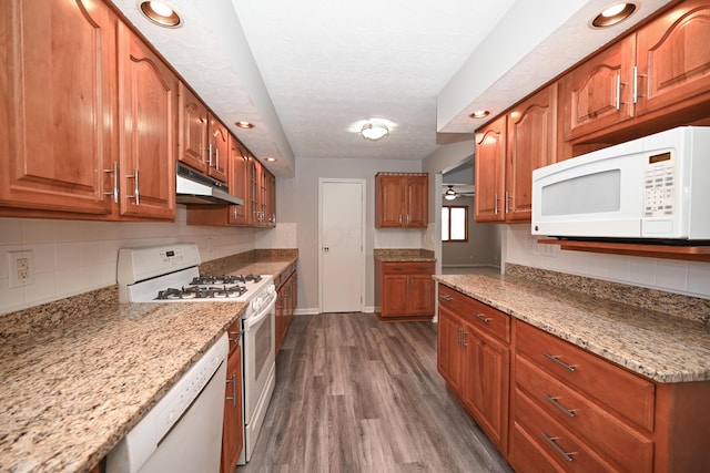 kitchen featuring brown cabinets, dark wood finished floors, backsplash, white appliances, and under cabinet range hood