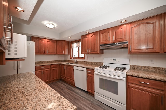 kitchen featuring dark wood-style floors, brown cabinetry, a sink, white appliances, and under cabinet range hood