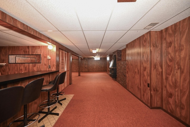 bar with wooden walls, visible vents, a paneled ceiling, carpet flooring, and a bar