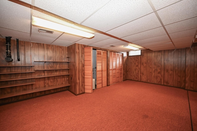 below grade area featuring carpet, visible vents, wood walls, and a paneled ceiling