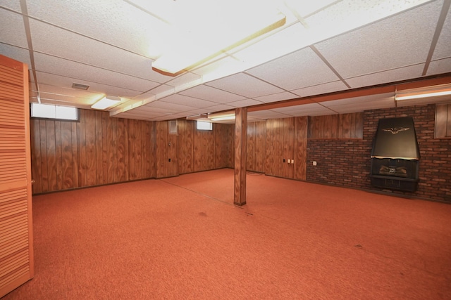 basement featuring carpet floors, a drop ceiling, and wooden walls