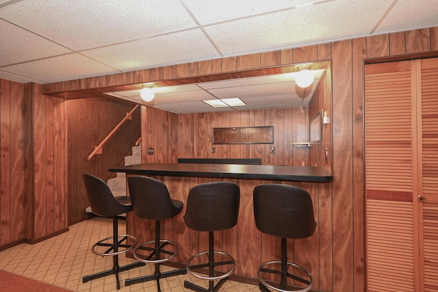 bar with a dry bar, stairs, wooden walls, and a paneled ceiling