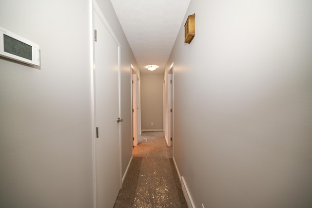 hall featuring a textured ceiling and baseboards