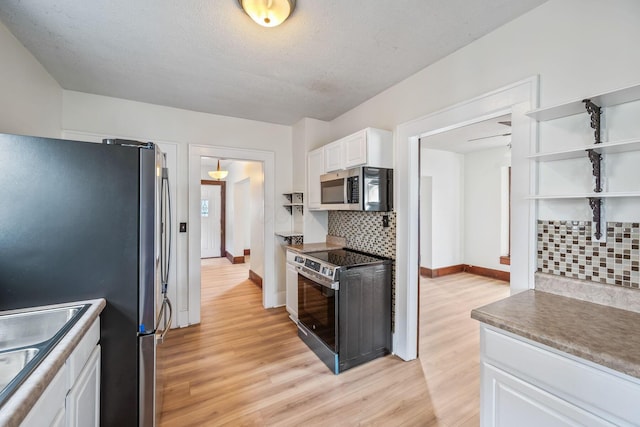 kitchen featuring stainless steel appliances, decorative backsplash, white cabinets, a sink, and light wood-type flooring