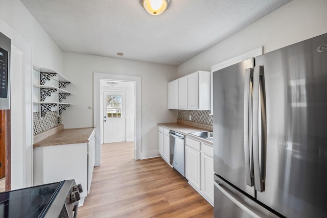 kitchen featuring light countertops, backsplash, light wood-style flooring, appliances with stainless steel finishes, and white cabinets