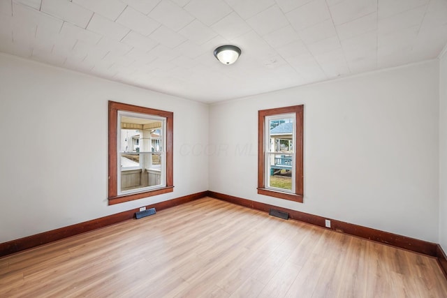 empty room featuring light wood-type flooring, visible vents, and baseboards