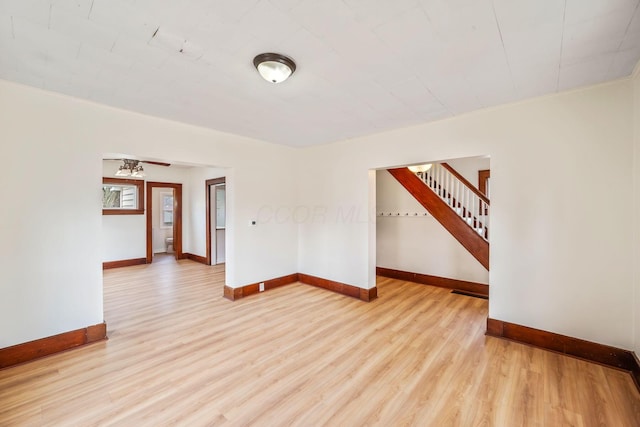 unfurnished room featuring baseboards, stairway, and light wood finished floors