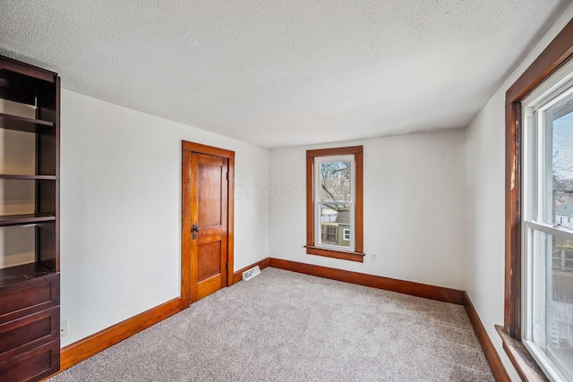 empty room with carpet flooring, visible vents, baseboards, and a textured ceiling