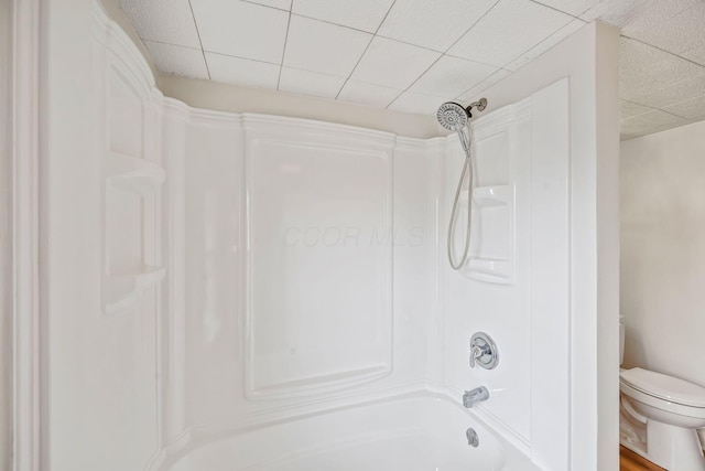 bathroom with washtub / shower combination, a paneled ceiling, and toilet