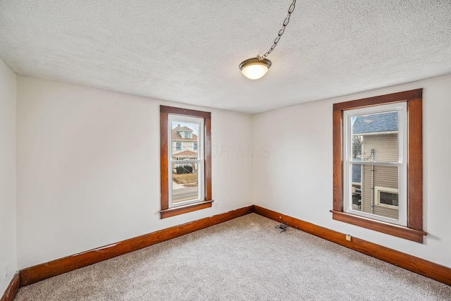 empty room with a textured ceiling, baseboards, and carpet flooring