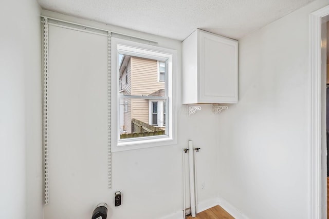 clothes washing area featuring a textured ceiling, cabinet space, and baseboards