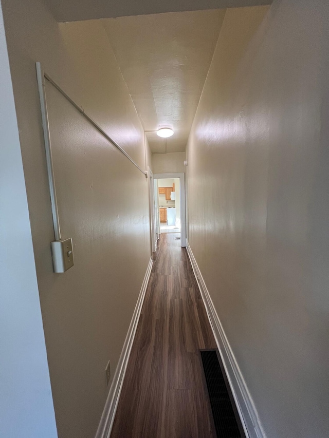 hallway with visible vents, baseboards, and dark wood-style flooring