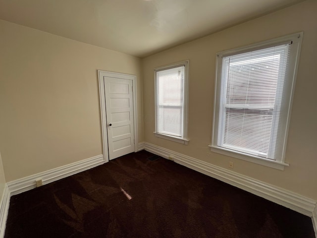 empty room featuring dark colored carpet and baseboards