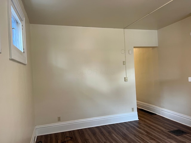 empty room featuring dark wood-style floors, baseboards, and visible vents