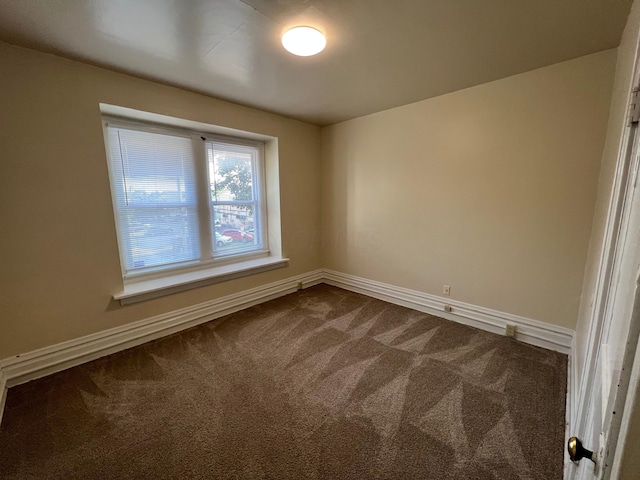 empty room featuring dark colored carpet and baseboards