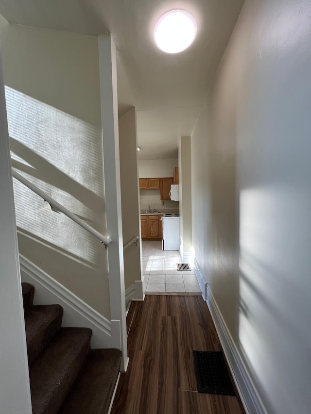 hallway featuring visible vents, stairway, light wood-style floors, a sink, and baseboards