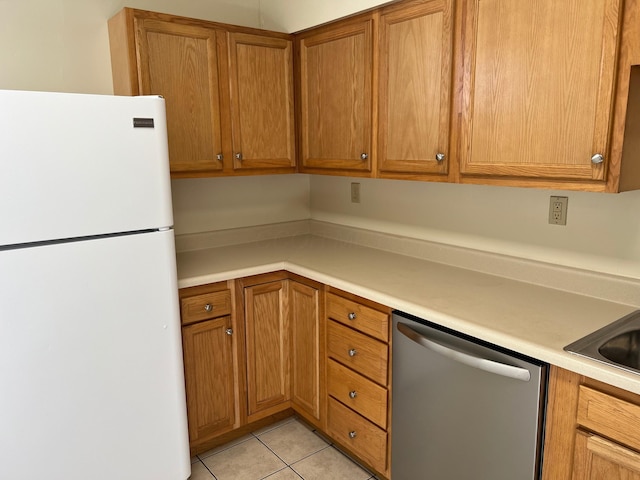 kitchen featuring light tile patterned floors, dishwasher, brown cabinets, freestanding refrigerator, and light countertops