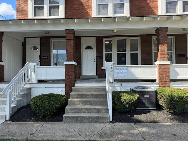 entrance to property featuring covered porch, brick siding, mansard roof, and central air condition unit