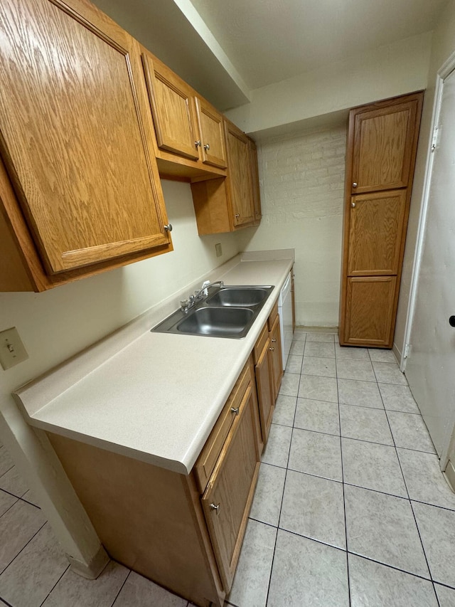 kitchen featuring white dishwasher, light tile patterned flooring, a sink, light countertops, and brown cabinetry